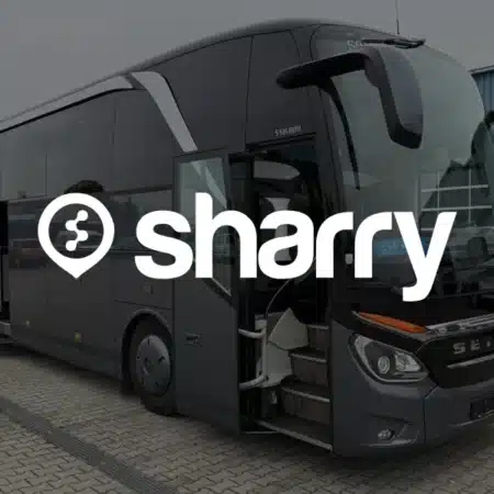 Czas to pieniądz. Dlaczego przeklikiwanie dziesięciu stron przewoźników to finansowa strata? | Sharry pl Logo i nazwa firmy sharry na tle otwartych przednich drzwi szarego autobusu